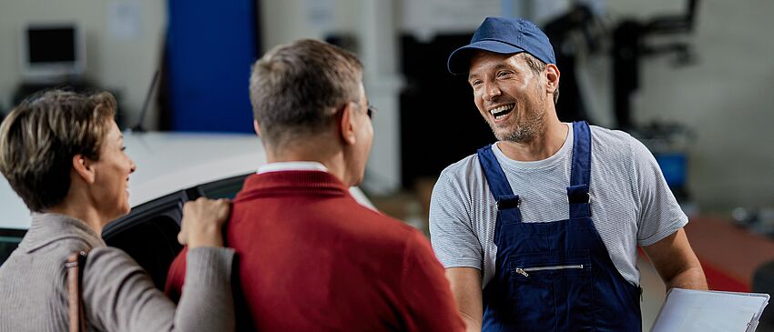 Glücklicher Automechaniker, der seinen Kunden in einer Werkstatt die Hand schüttelt - Zum Beitrag